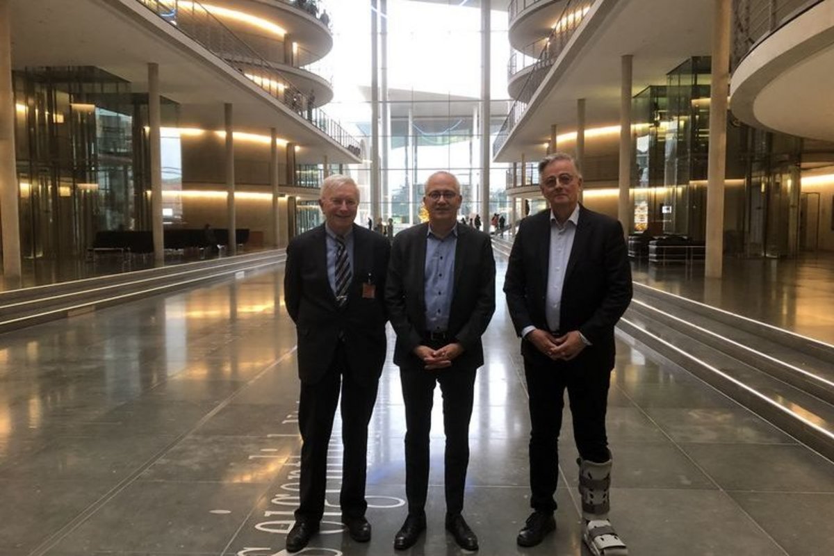 3 Männer in dunklen Anzügen in einer Halle